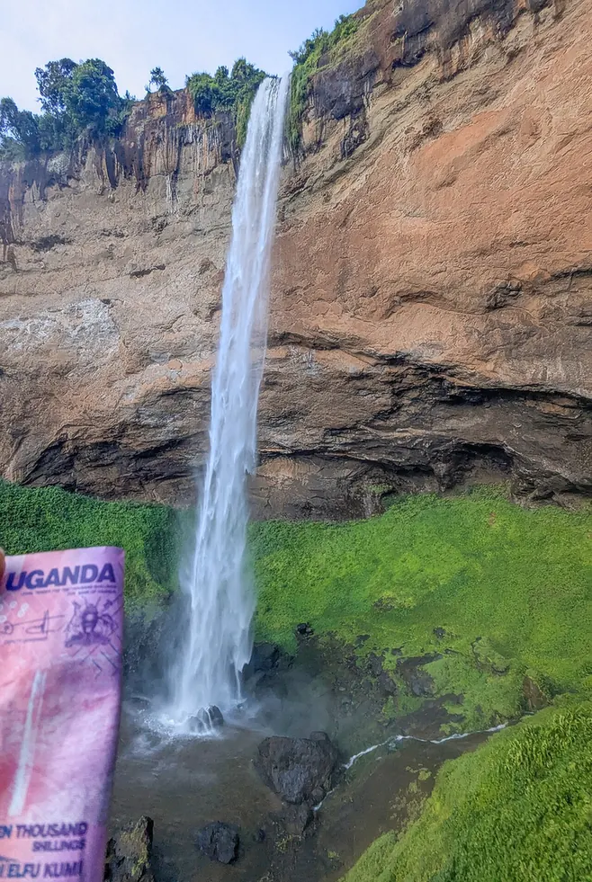 A Ugandan 10,000-shilling note photographed in front of the Sipi Falls it depicts.