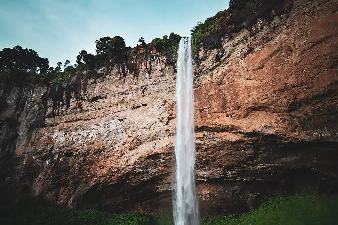 A tall cascade falling past a rock cliff at Sipi Falls, Uganda.